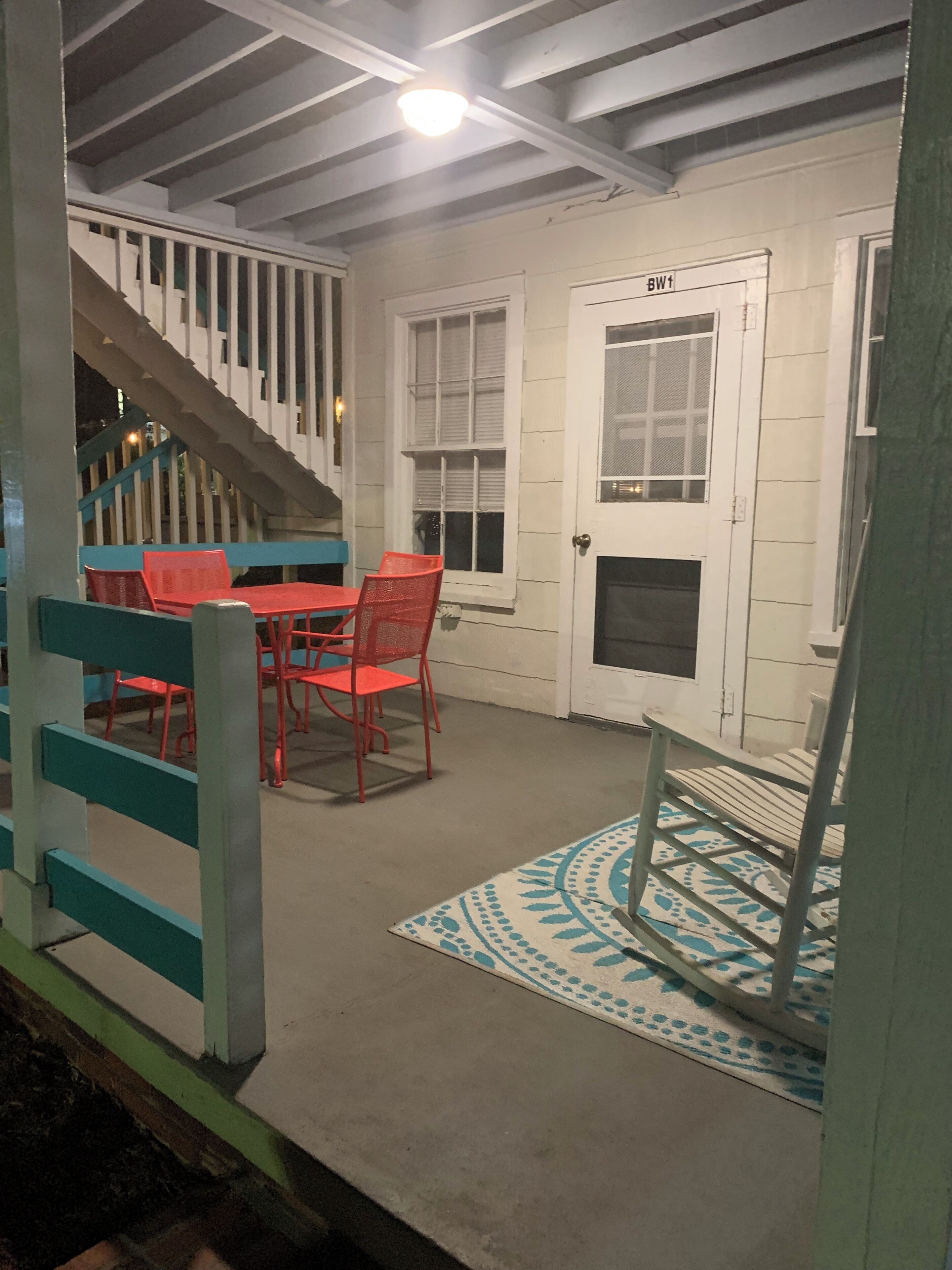 Uma área externa coberta com escadas, uma mesa com cadeiras e um tapete estampado.