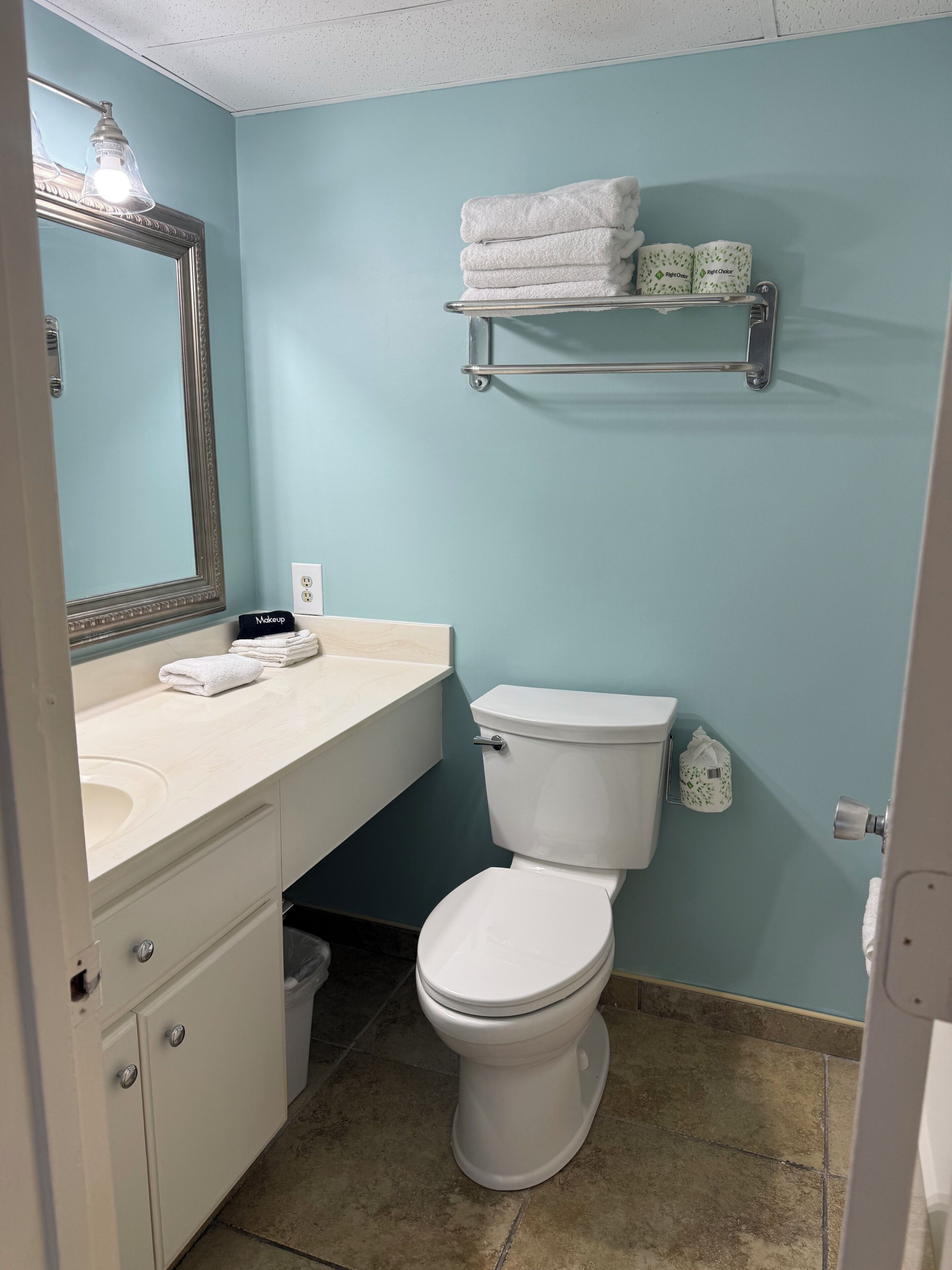 Une salle de bain avec des toilettes, un lavabo et un miroir. Des serviettes sont pliées et empilées sur une étagère au-dessus des toilettes.