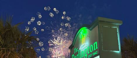 A sign for 'The Darlington' with a 'Happy Birthday America' message, palm trees, and a street view with parked cars and a police SUV.