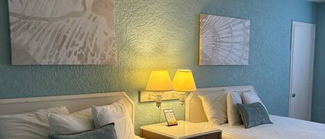 A hotel room with two beds, a nightstand with lamps, and artwork on the walls.