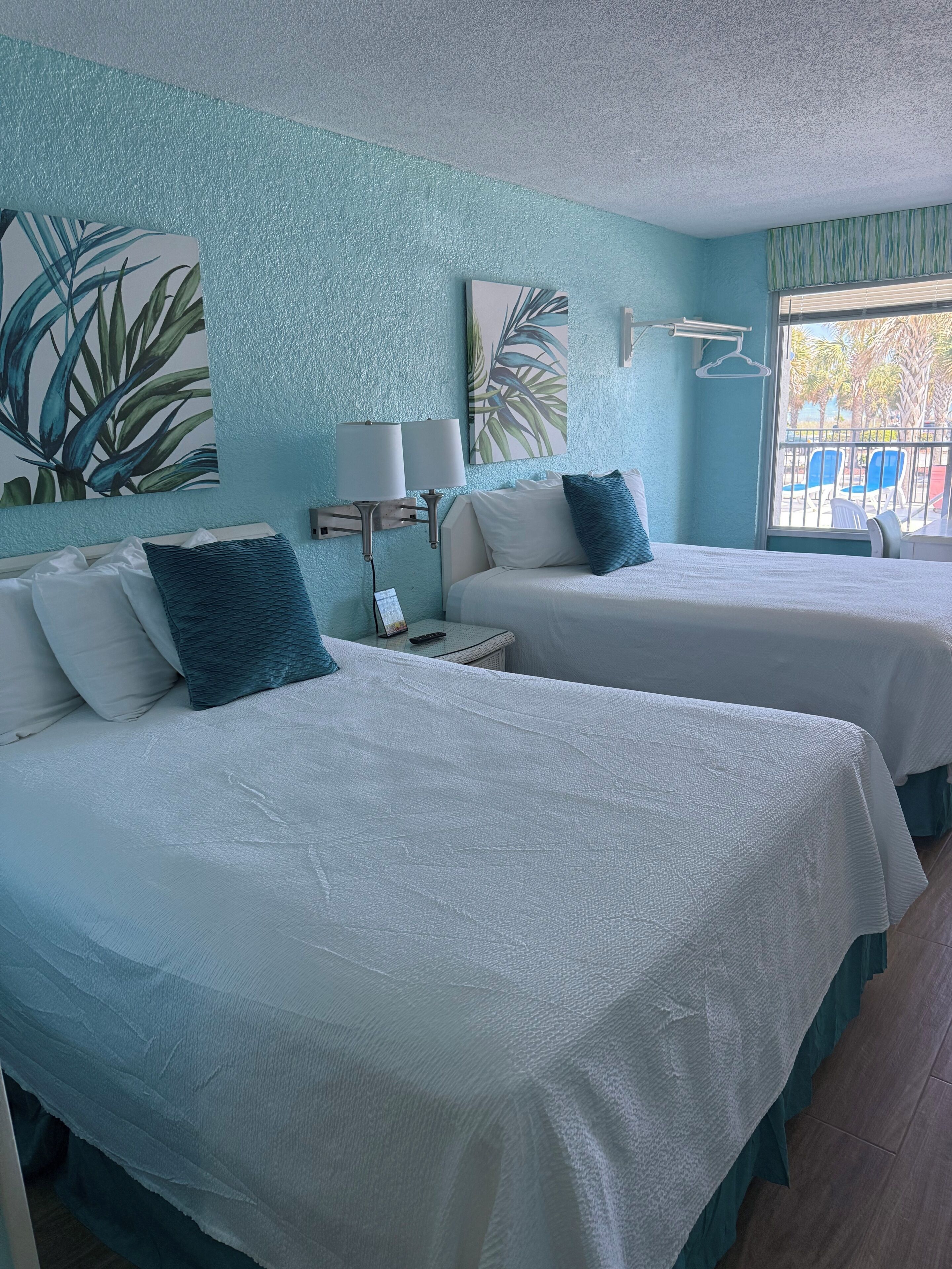 A hotel room with two beds, a window with a view, and wall art.