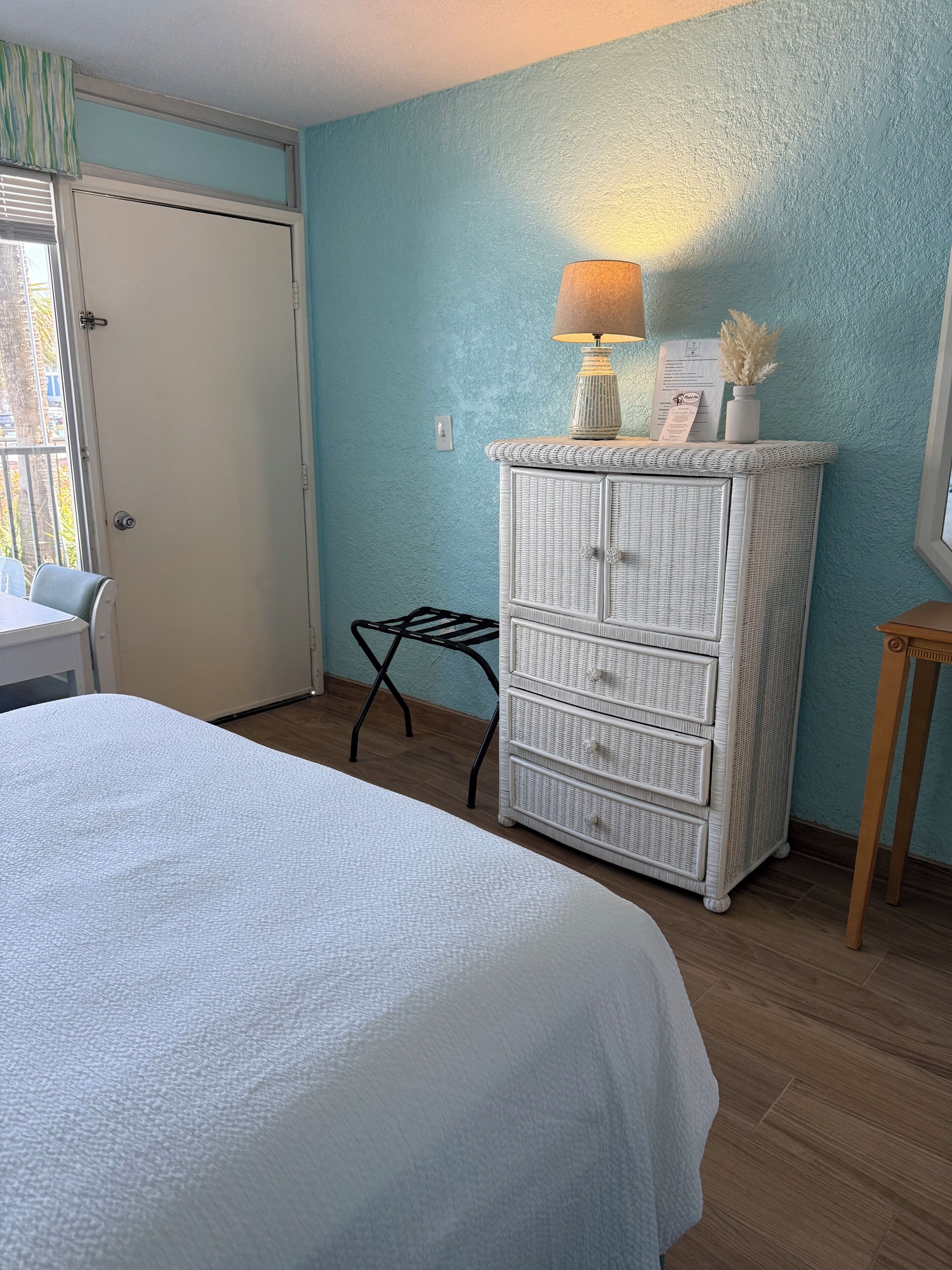 A room with a bed, a white dresser, a small table, and a chair.