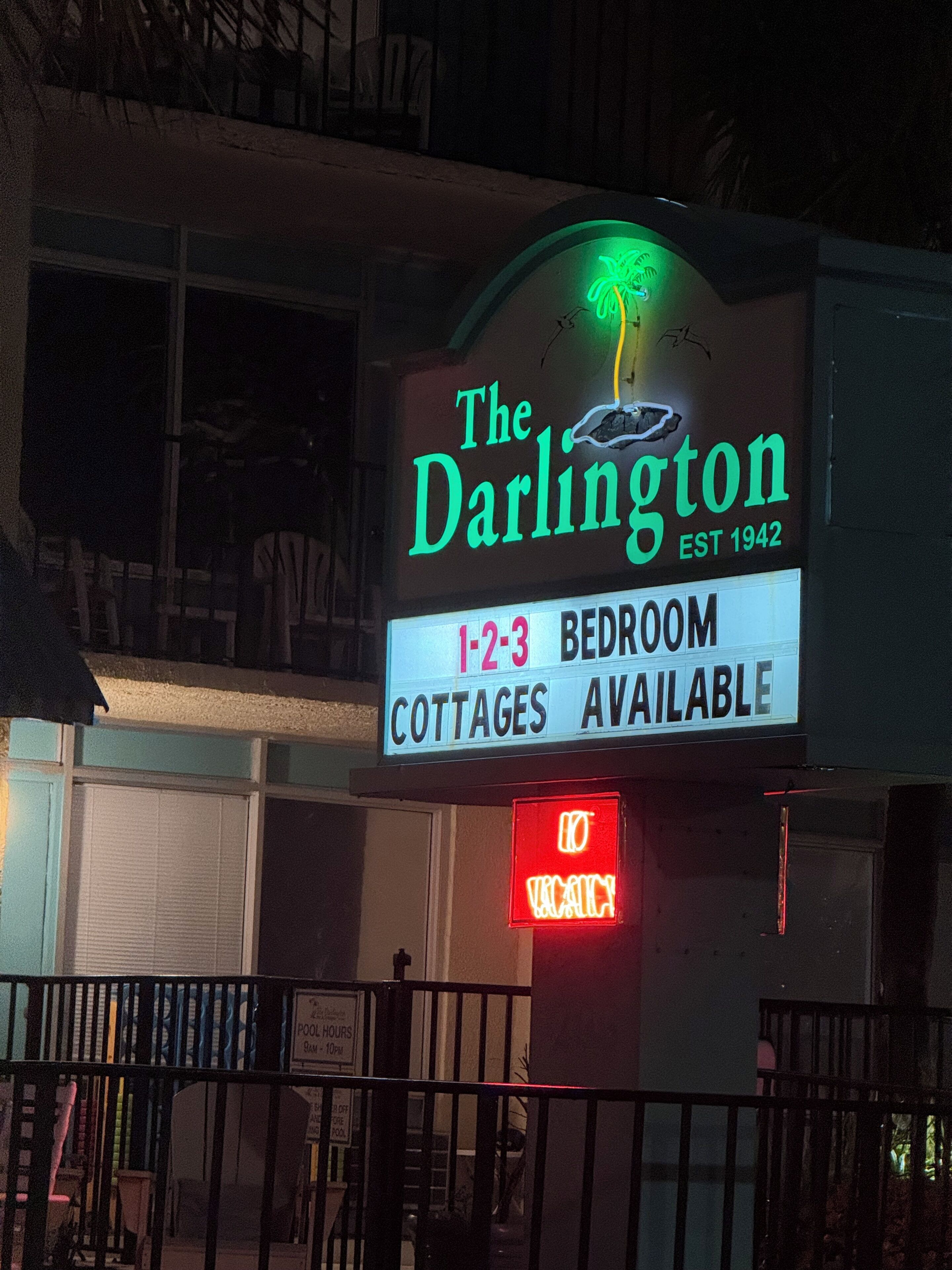 Schild für das Hotel 'The Darlington' mit einer Neon-Palme, das Cottages mit 1, 2 oder 3 Schlafzimmern ankündigt.