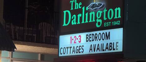 A sign for 'The Darlington' hotel with a neon palm tree, indicating 1-2-3 bedroom cottages available.