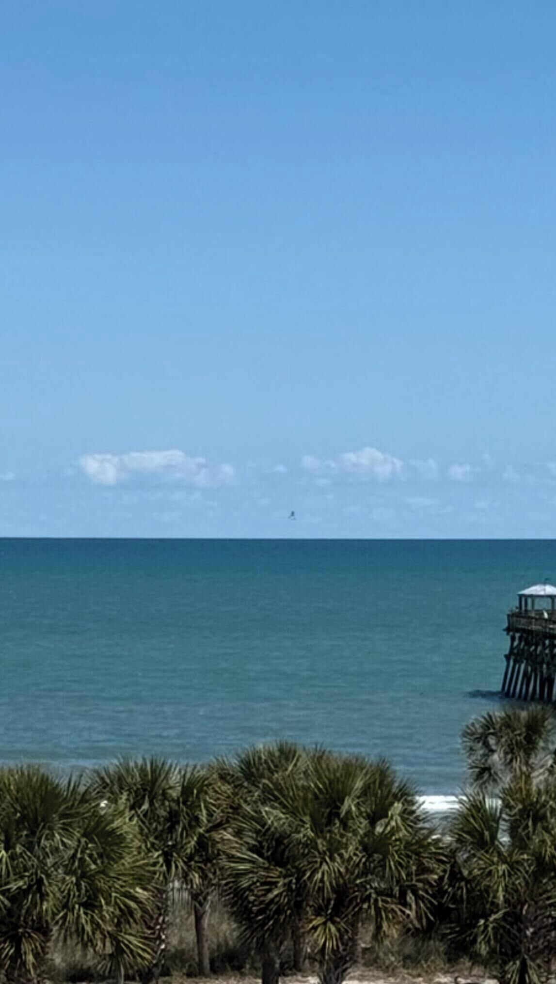 A coastal view with a clear sky, a body of water, and a pier structure.