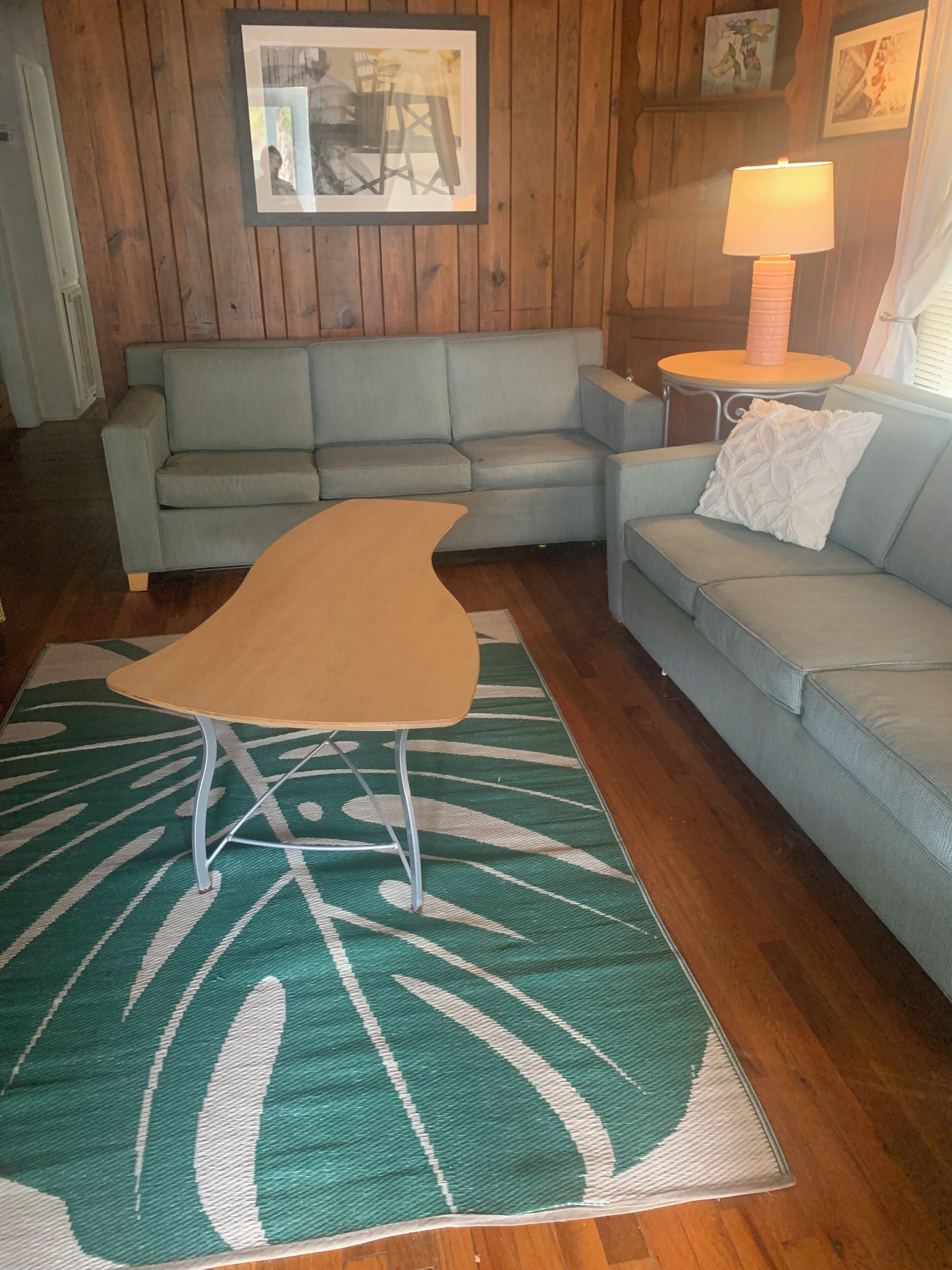A living room with a sofa, a coffee table, a patterned rug, wooden walls, and a lamp.