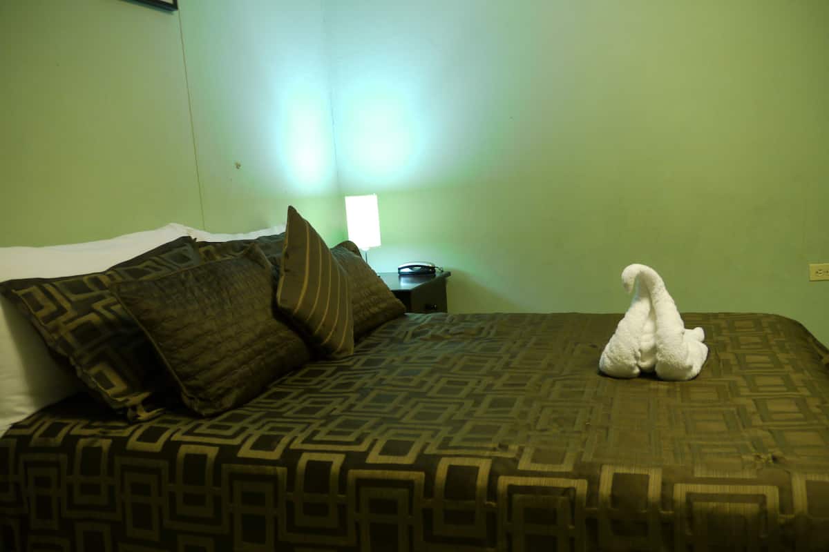 A hotel room with a bed, pillows, a nightstand, and a lamp.