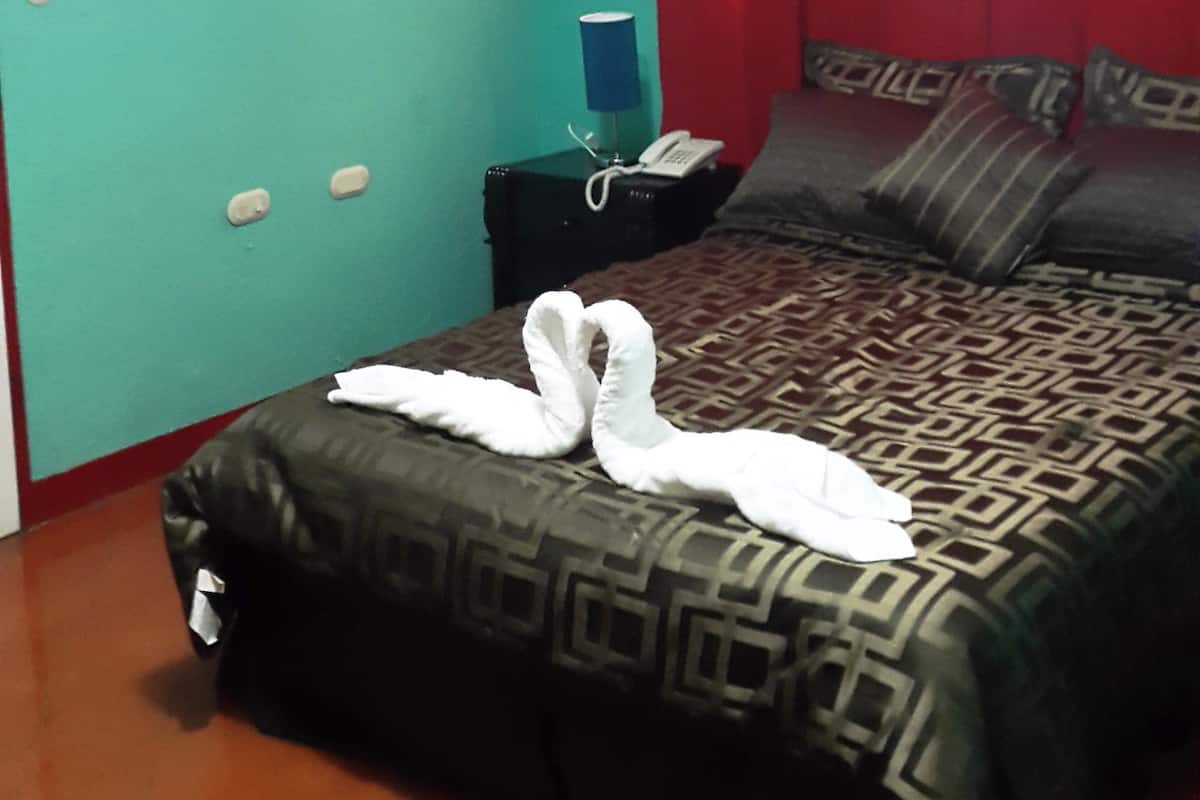 A hotel room with a bed, a nightstand, an air conditioner, a telephone, and a red curtain.