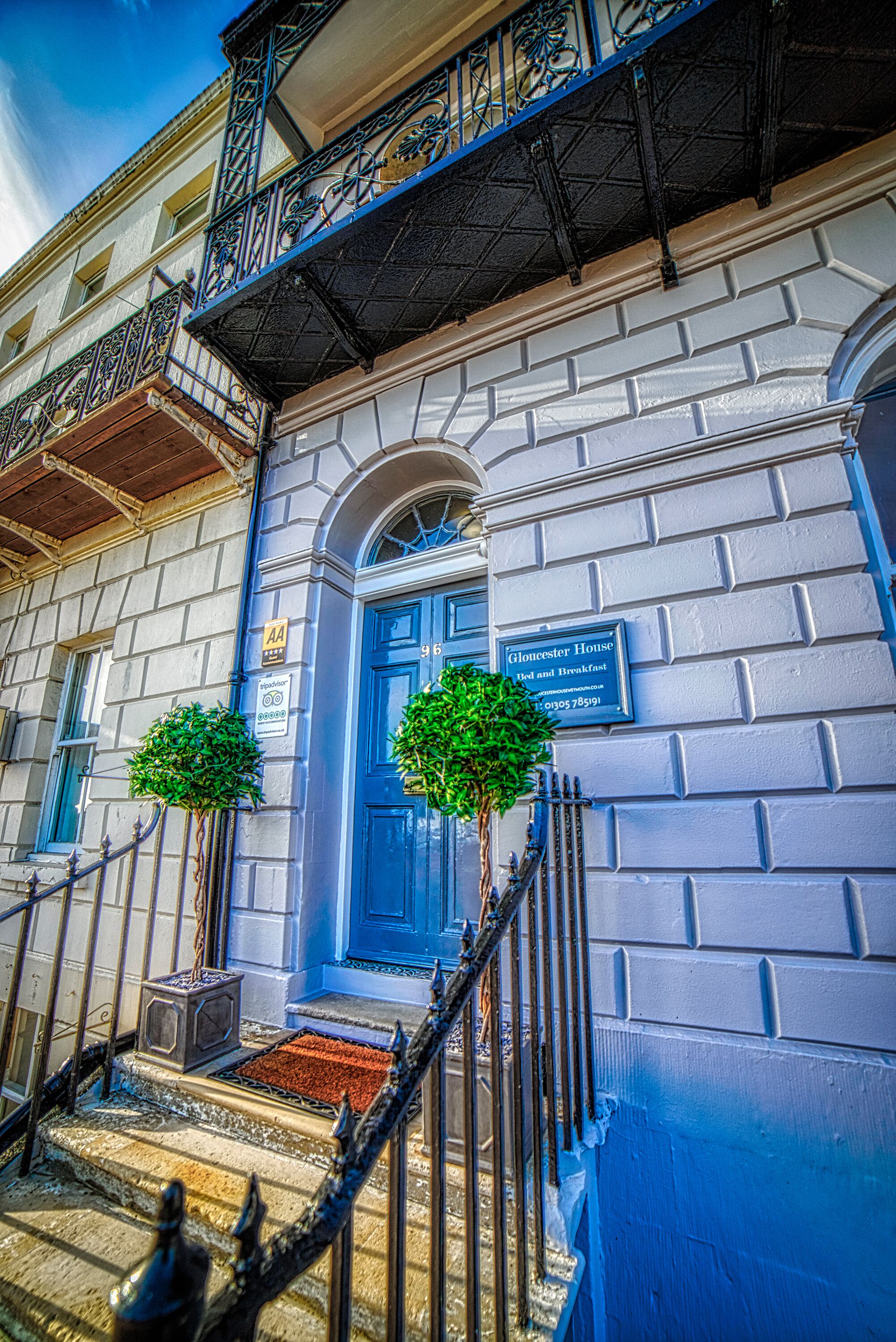 Un edificio con una porta blu, un cartello con la scritta 'Glencester House Bed and Breakfast' e due piccoli alberi davanti alla scalinata.