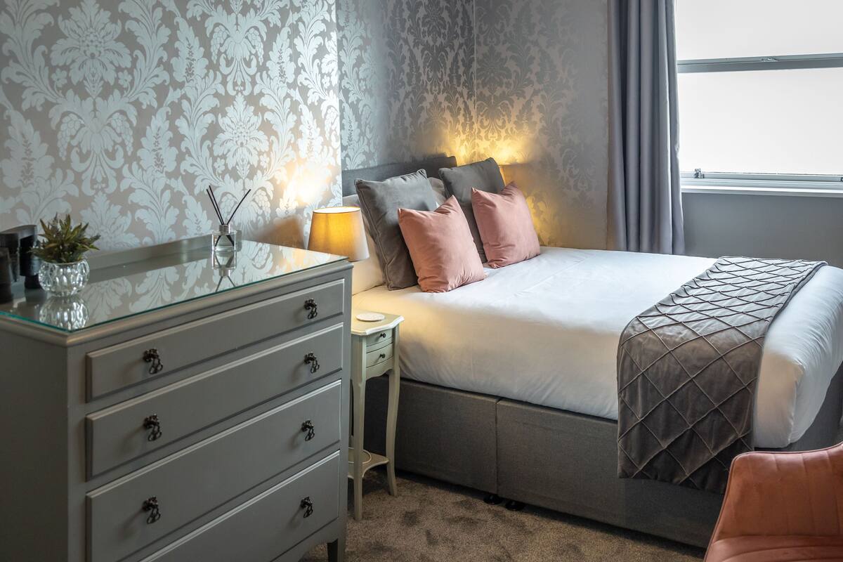 Un dormitorio con cama, mesita de noche, cómoda y ventana con cortinas.