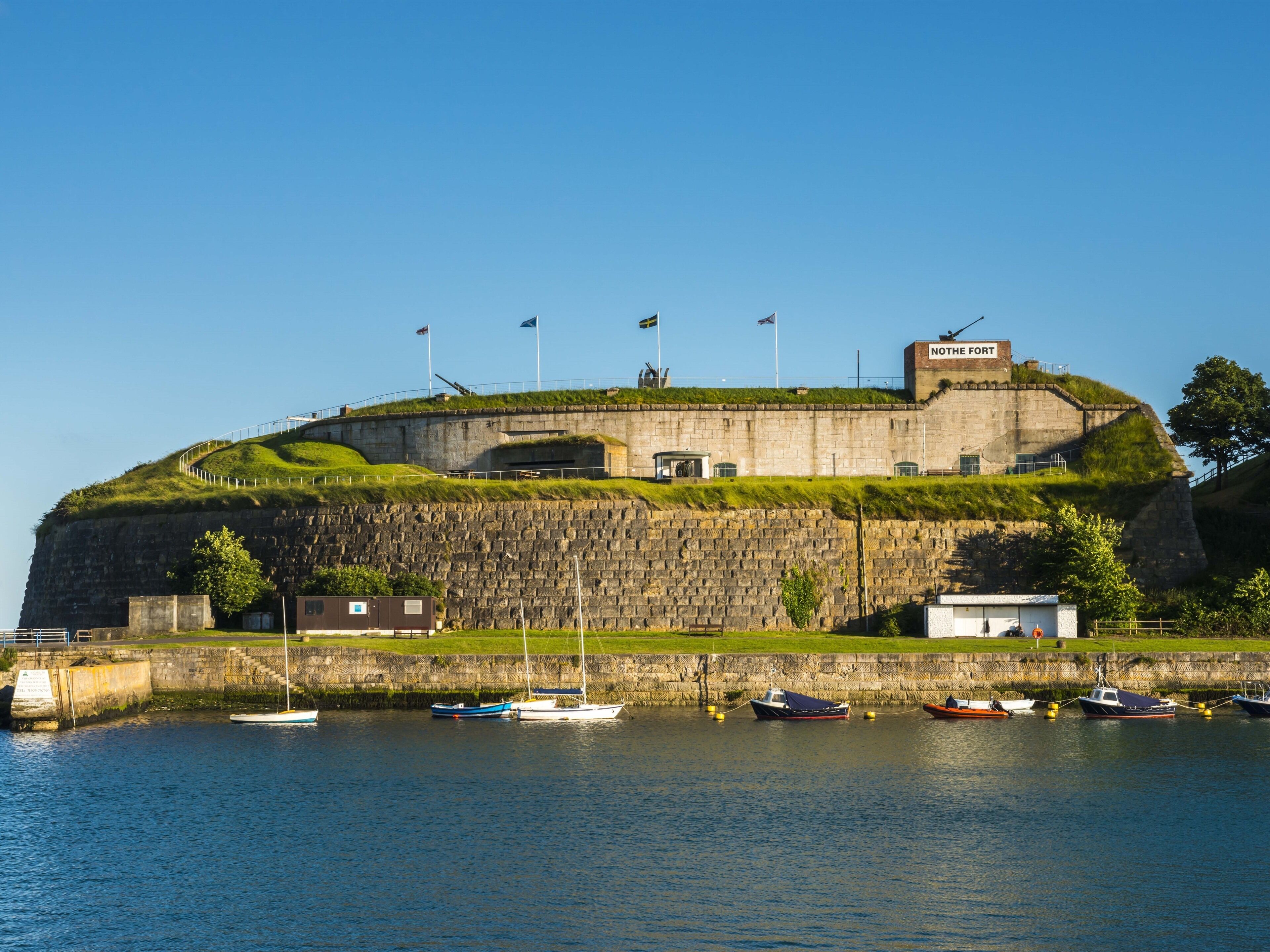 A historic fort with a grassy top, a stone wall, and a clear blue sky.