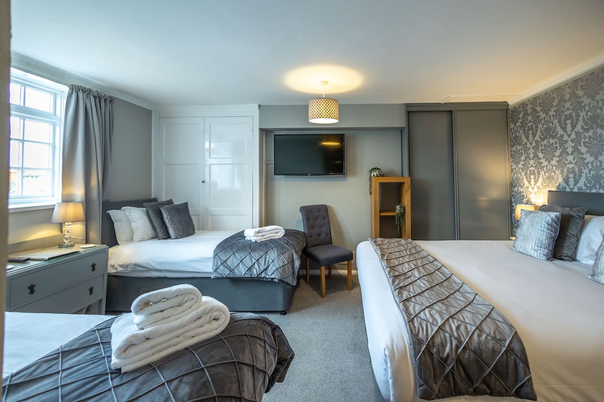 Habitación de hotel con dos camas, televisión, escritorio con lámpara y ventana con cortinas.