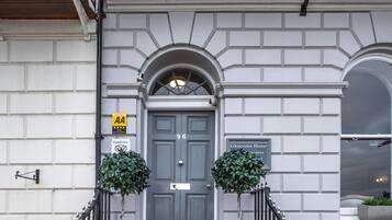 A grand entrance with a grey door, a staircase with a black railing, and two potted plants on either side.