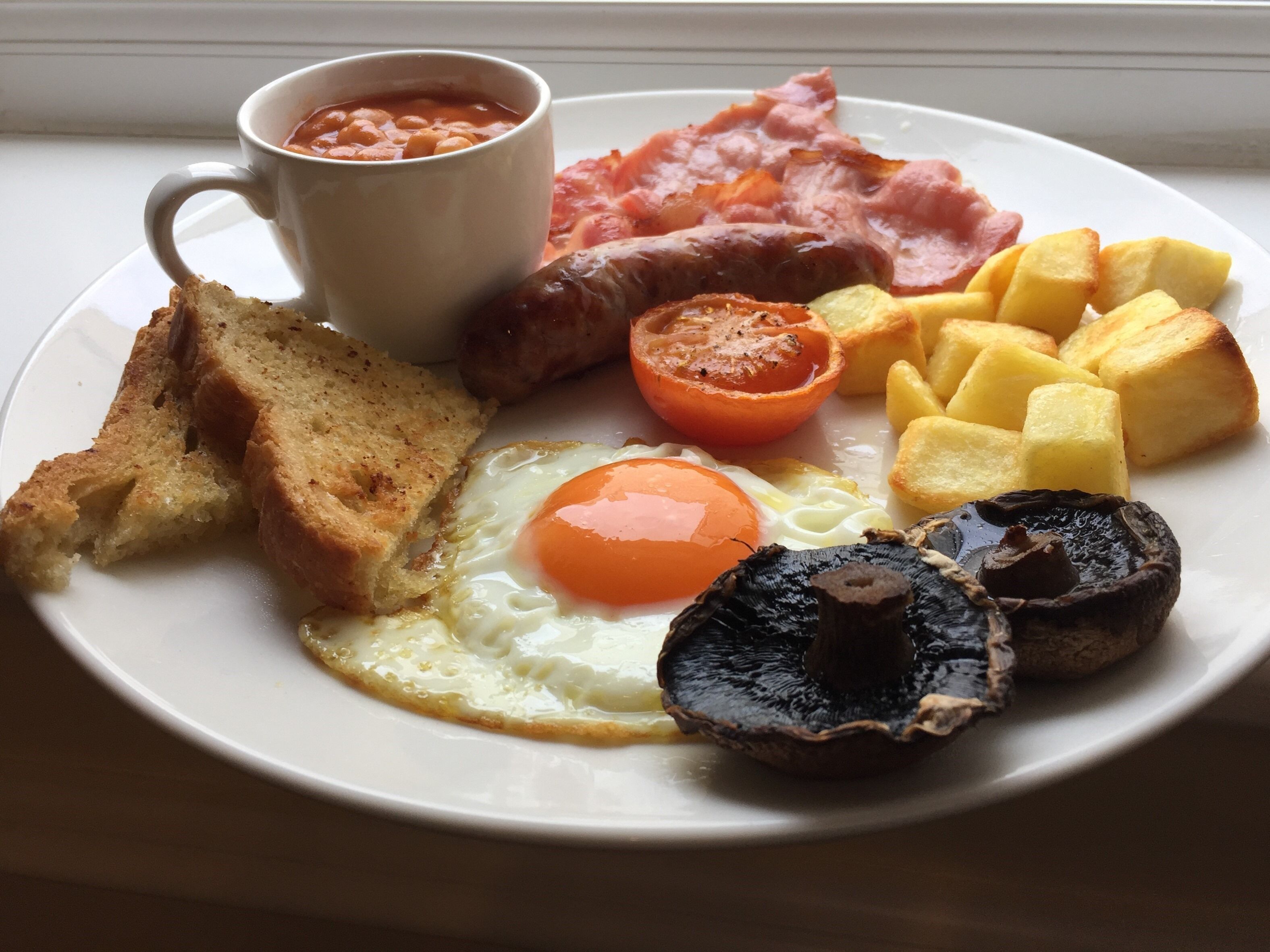 A plate of breakfast food including eggs, bacon, tomatoes, toast, and beans.