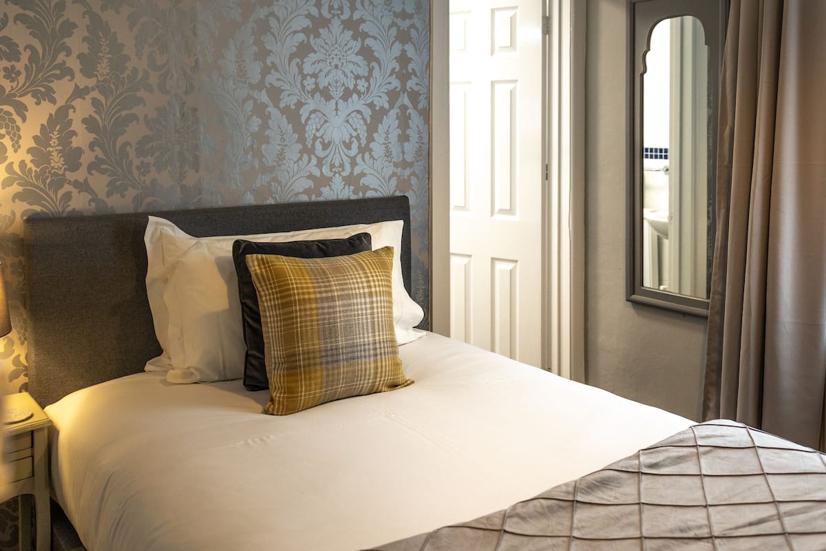 Una cama bien hecha con cabecera, lámpara de noche y ventana con cortinas.