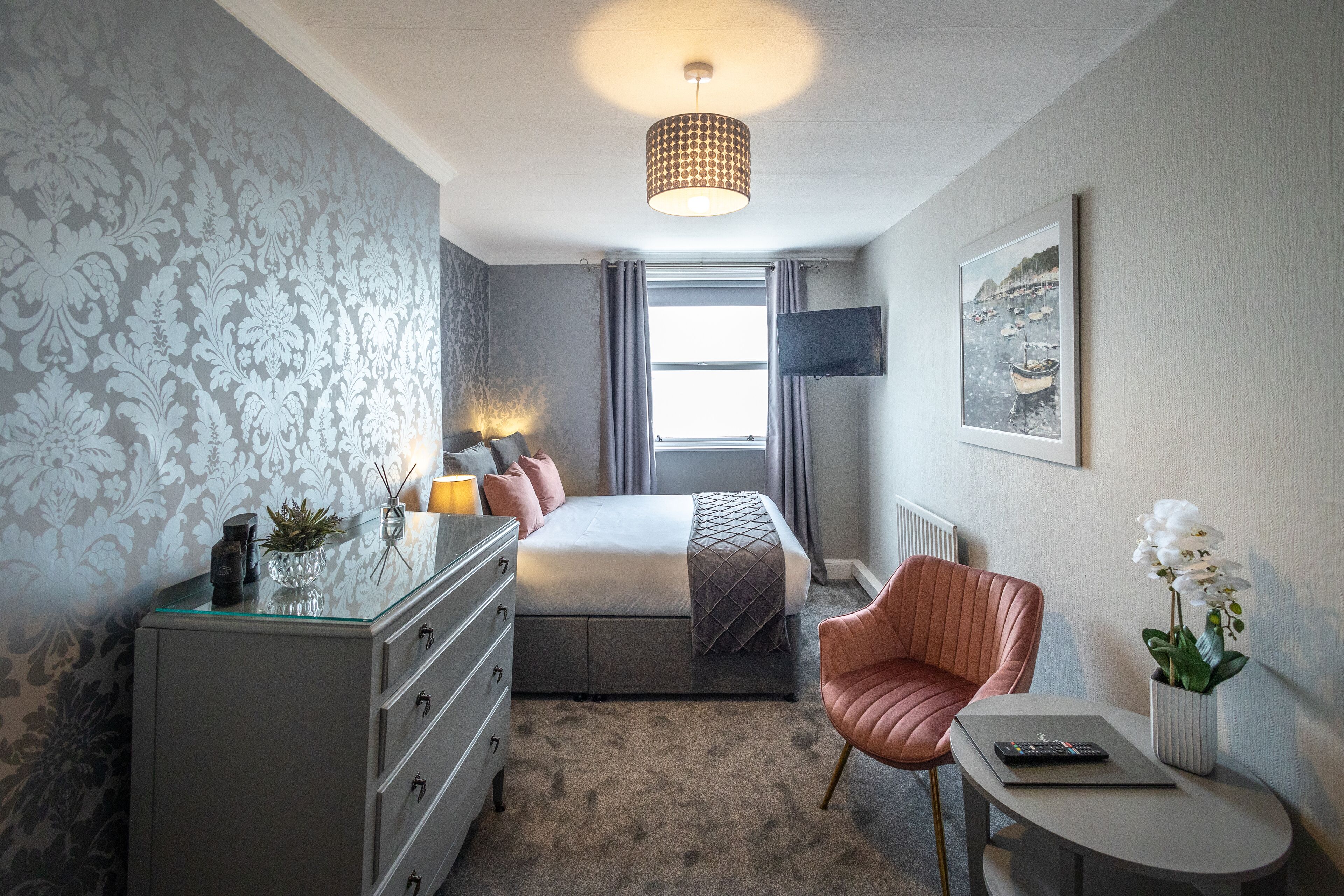 A bedroom with a bed, dresser, chair, table, and a window with curtains.