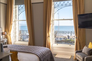 A hotel room with a bed, a desk, a chair, a TV, and a balcony with a view of the sea. - Gloucester House (Weymouth)