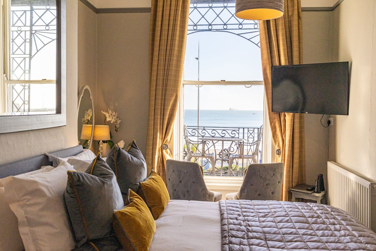 Habitación de hotel con cama, dos sillones, televisor y vista al mar desde el balcón.