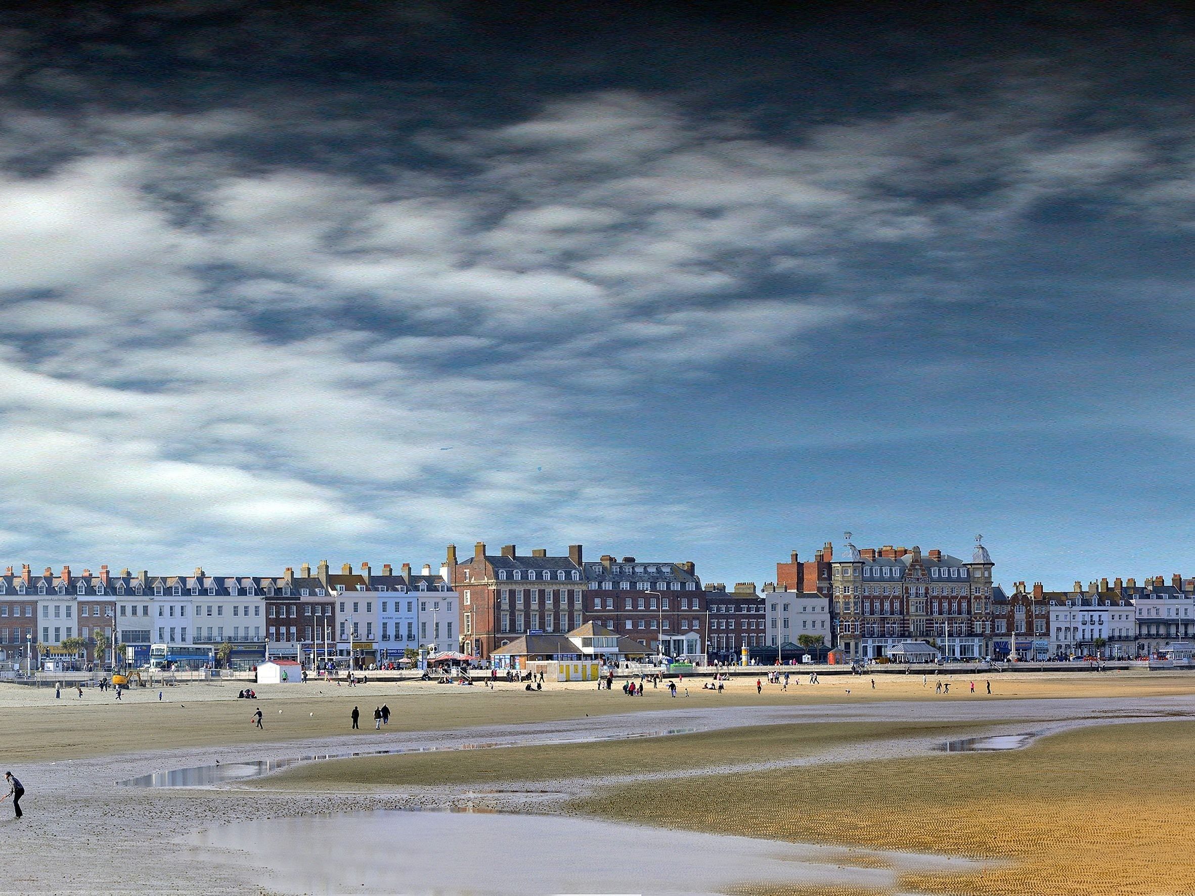 A coastal town with a beach, buildings, and a cloudy sky.