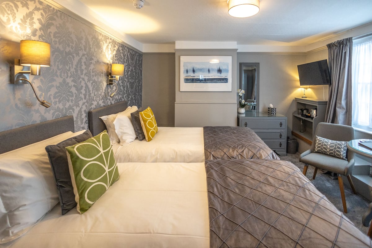 Habitación de hotel con dos camas, un escritorio, una silla, un televisor y un cuadro en la pared.