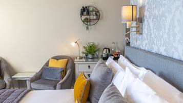 A modern hotel room with a bed, a chair, a nightstand, a lamp, and a wall-mounted shelf.