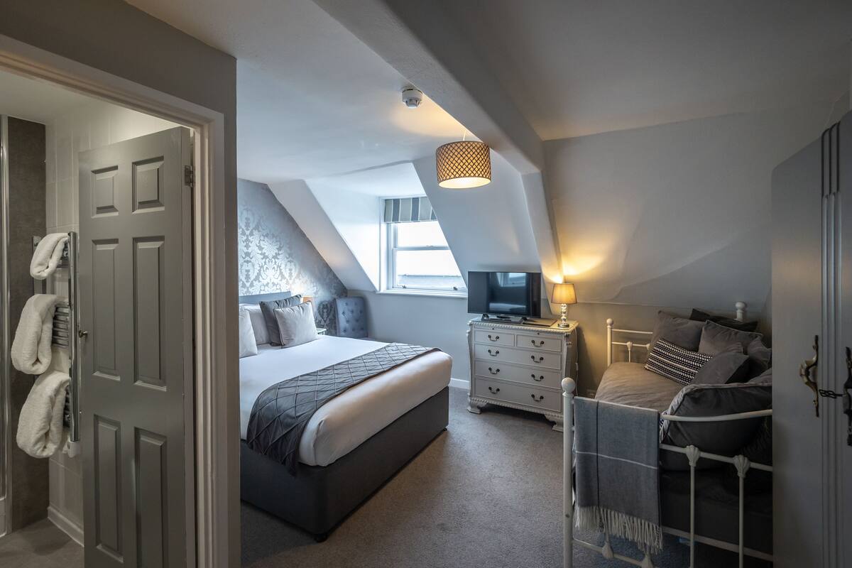 Un dormitorio con una cama, un aparador, un televisor y una ventana.
