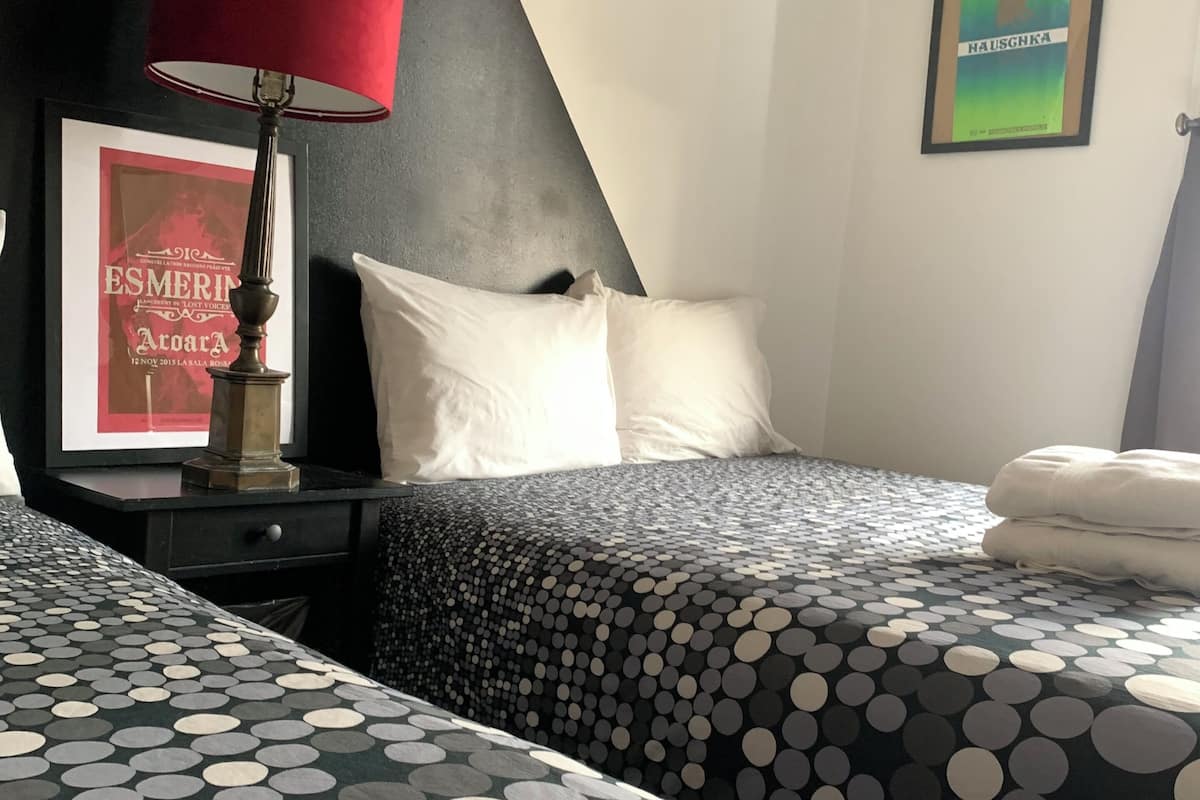 A hotel room with two beds, a nightstand, a lamp, a framed picture, and an air conditioning unit.