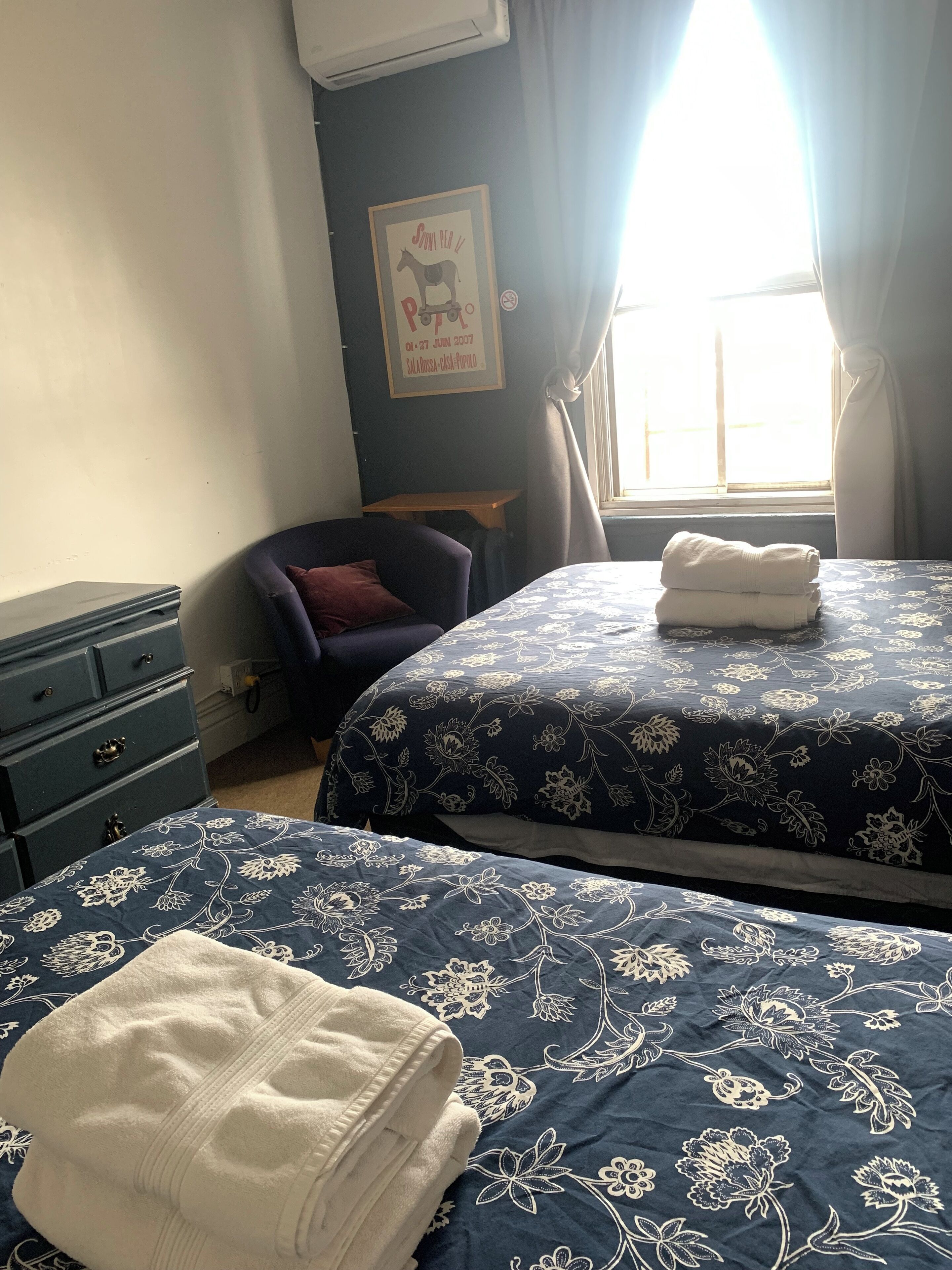 A hotel room with two beds, a small desk, a chair, and a window with curtains.