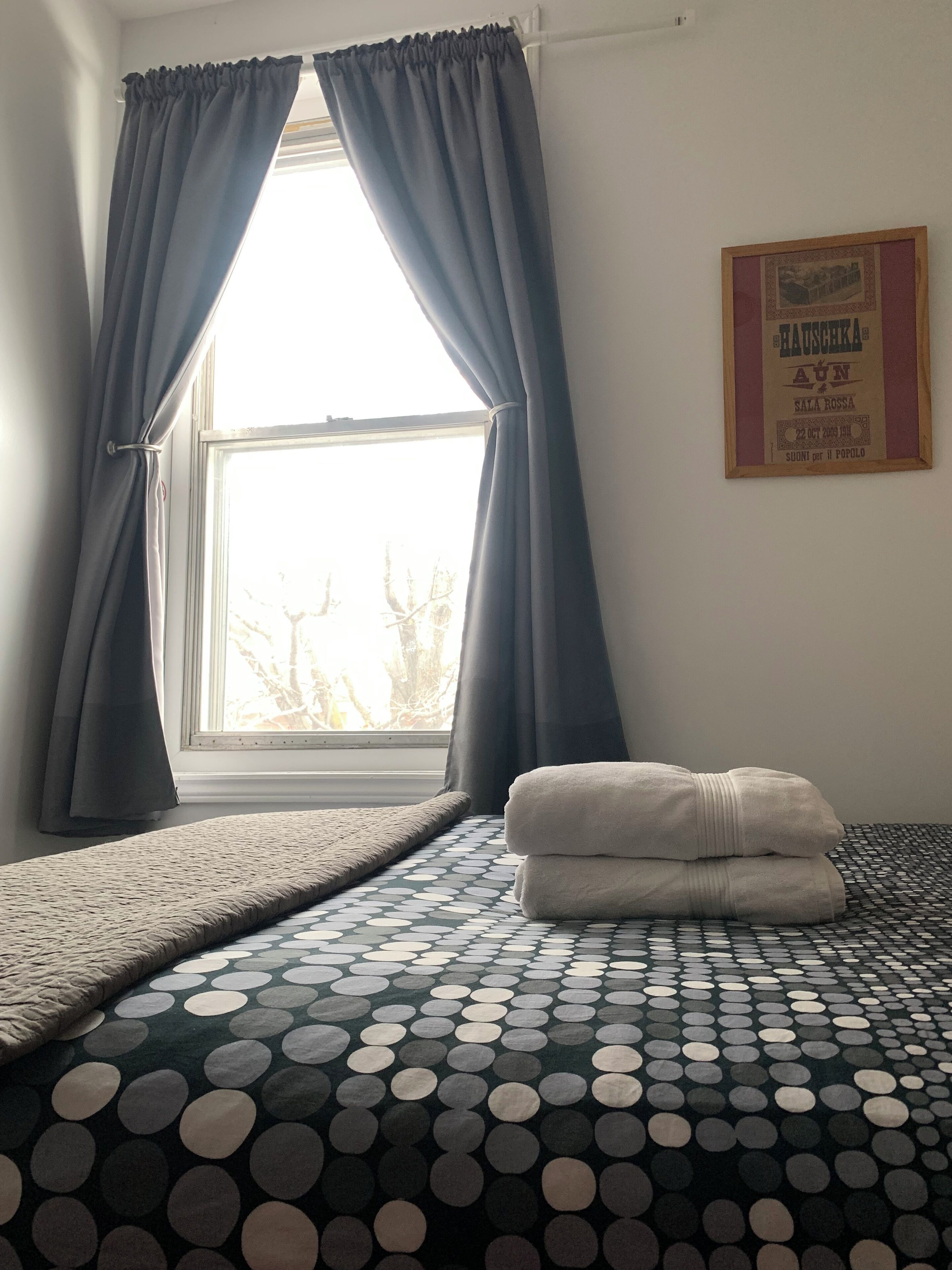 A room with a bed, a window with curtains, a framed picture on the wall, and a patterned bedspread.