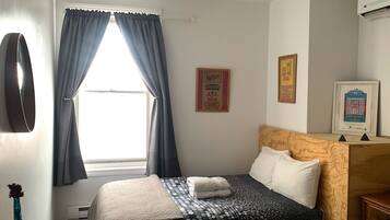 A hotel room with two beds, a wooden desk, a blue vase, and a window with curtains.