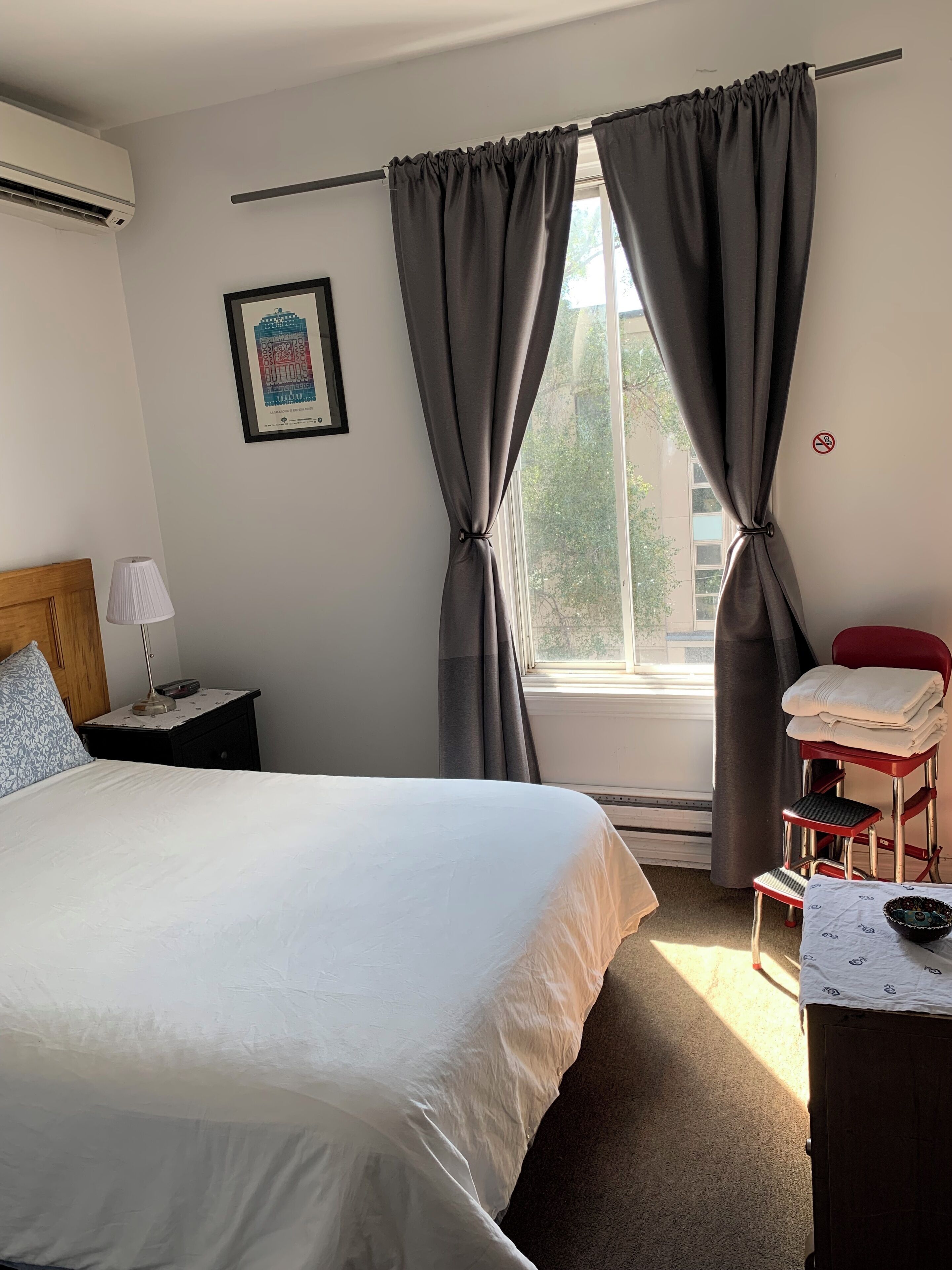 A hotel room with a bed, a nightstand with a lamp, a chair, and a window with curtains.