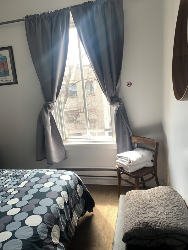 Une chambre à coucher avec un lit, une chaise sur laquelle sont pliées des serviettes, une fenêtre avec des rideaux et un tableau encadré accroché au mur.