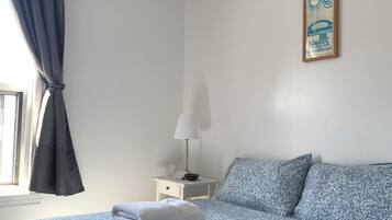 Una cama bien hecha con estampado floral, una mesita de noche con una lámpara y un cuenco, y un póster enmarcado en la pared.