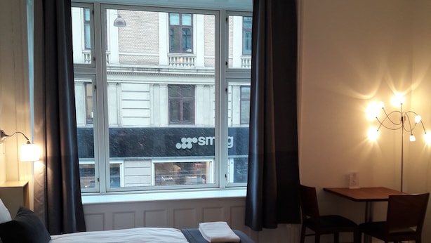 A hotel room with two beds, a dining table, and a view of a building with a sign that reads "sm". - Hotel Loeven (Copenhagen)
