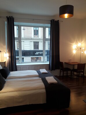 A hotel room with two beds, a dining table, and a view of a building with a sign that reads "sm".