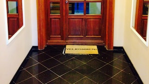 A wooden double door with glass panels, a doormat with "VELKOMMEN!" written on it, and black tiled flooring. - Hotel Loeven (Copenhagen)