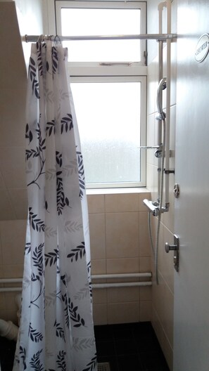 A bathroom with a shower curtain, a window, and a shower head.