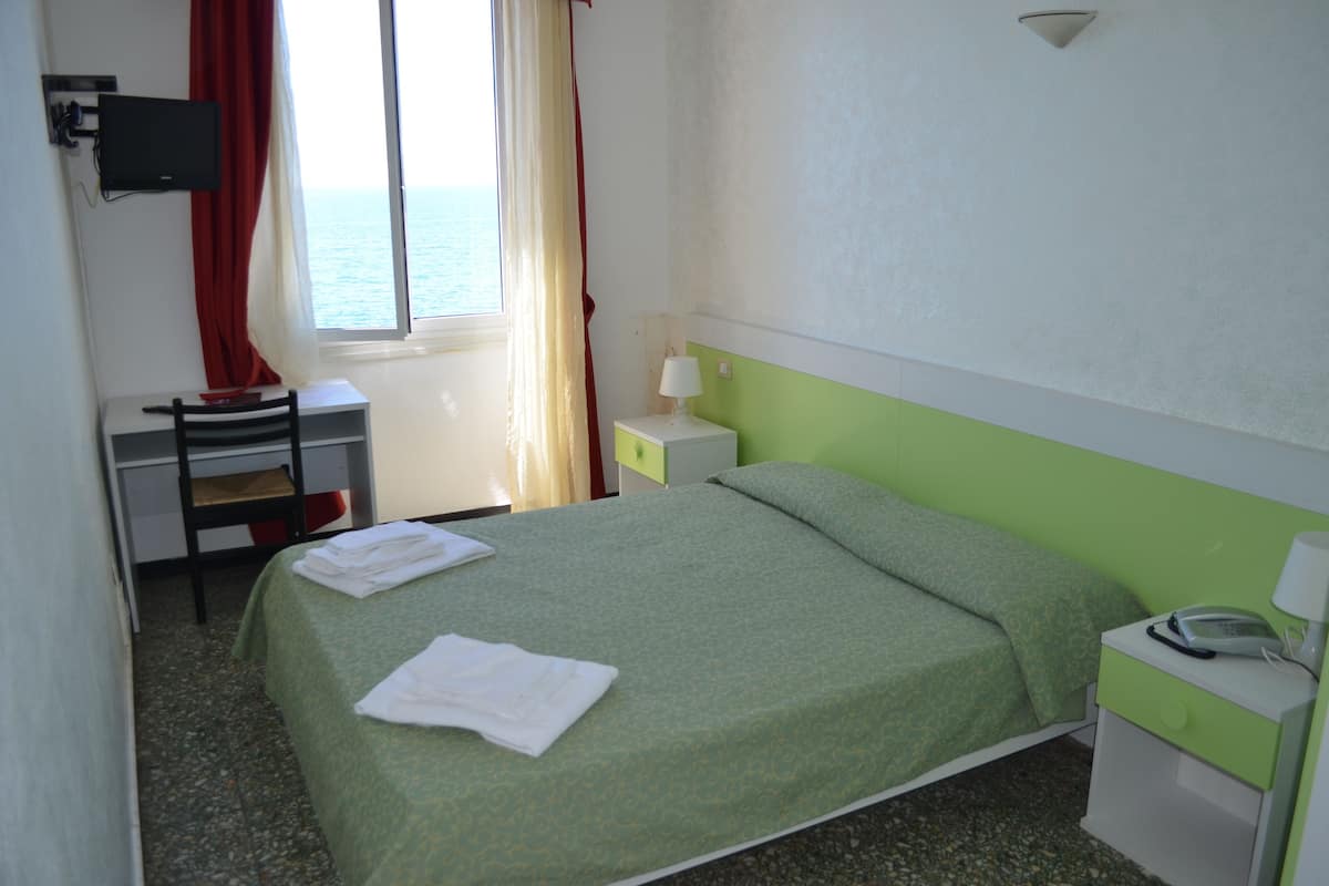 A room with a bed, a desk, a chair, a nightstand, a lamp, and a TV.