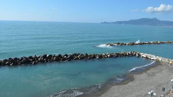 A coastal beach with a rocky breakwater and a clear view of the sea and distant mountains.