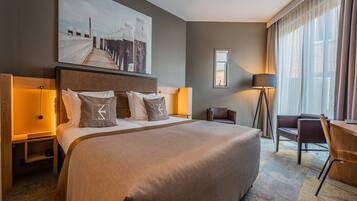 Een hotelkamer met een groot bed, een bureau, een stoel, een lamp en een schilderij aan de muur.