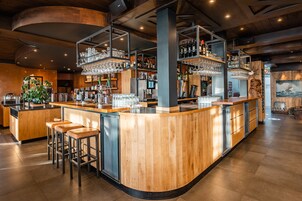 Un área de bar moderna con mostradores de madera, taburetes y estanterías llenas de vasos y botellas.
