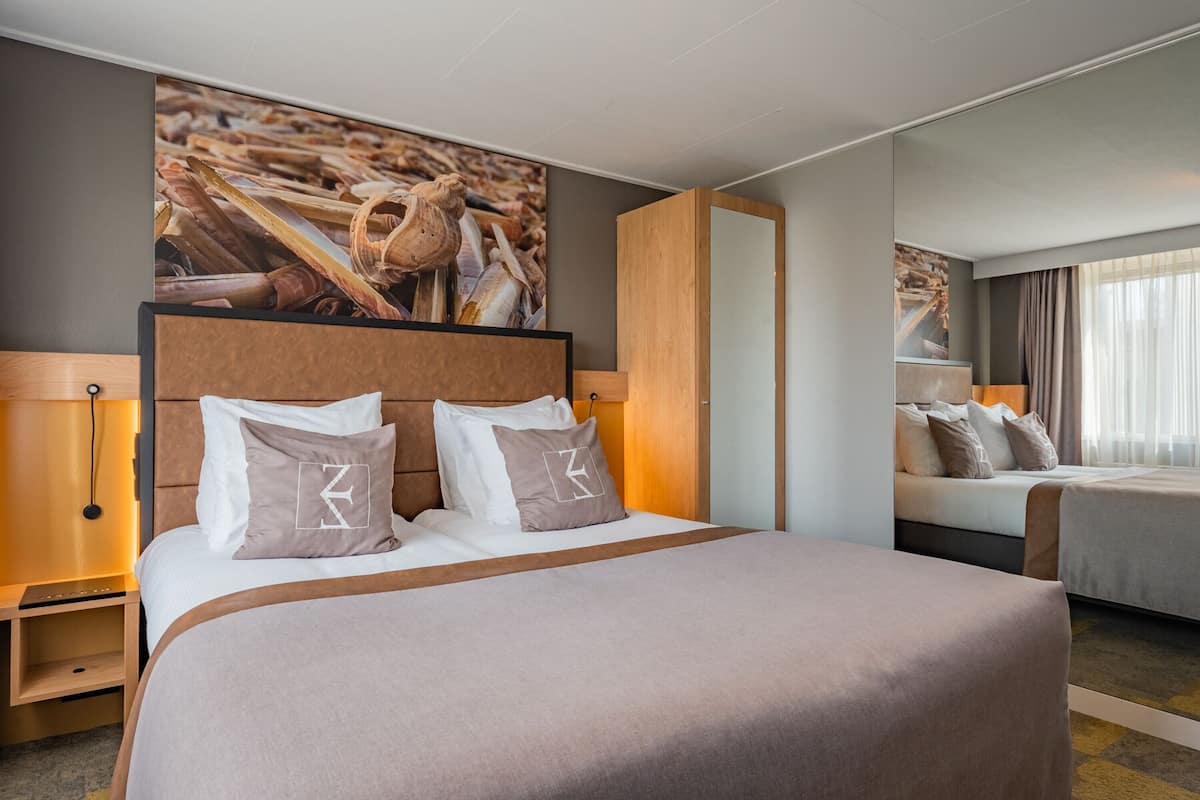 A hotel room with a large bed, two bedside tables, a nightstand, a mirror, and a large painting on the wall.