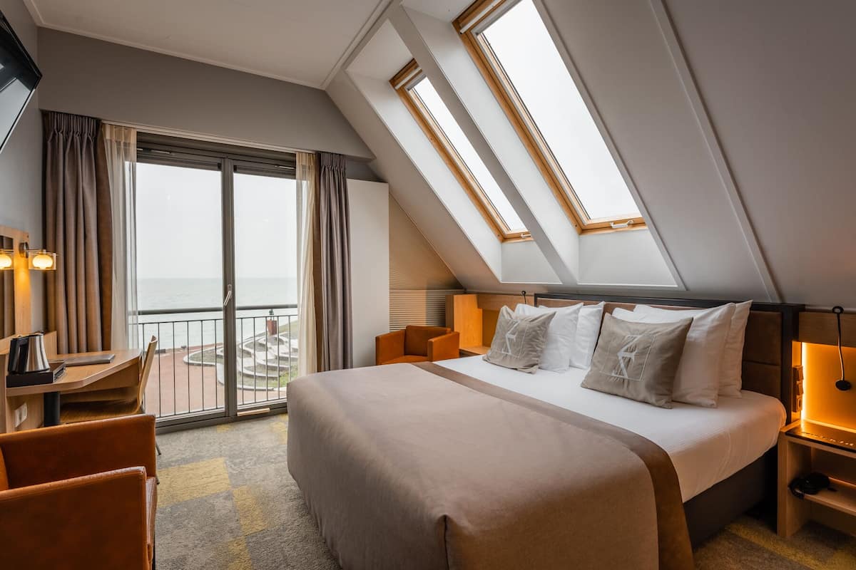 A hotel room with a large bed, a desk, and a view of the sea through a balcony.