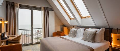 Et hotelværelse med en stor seng, et skrivebord og havudsigt fra en balkon.