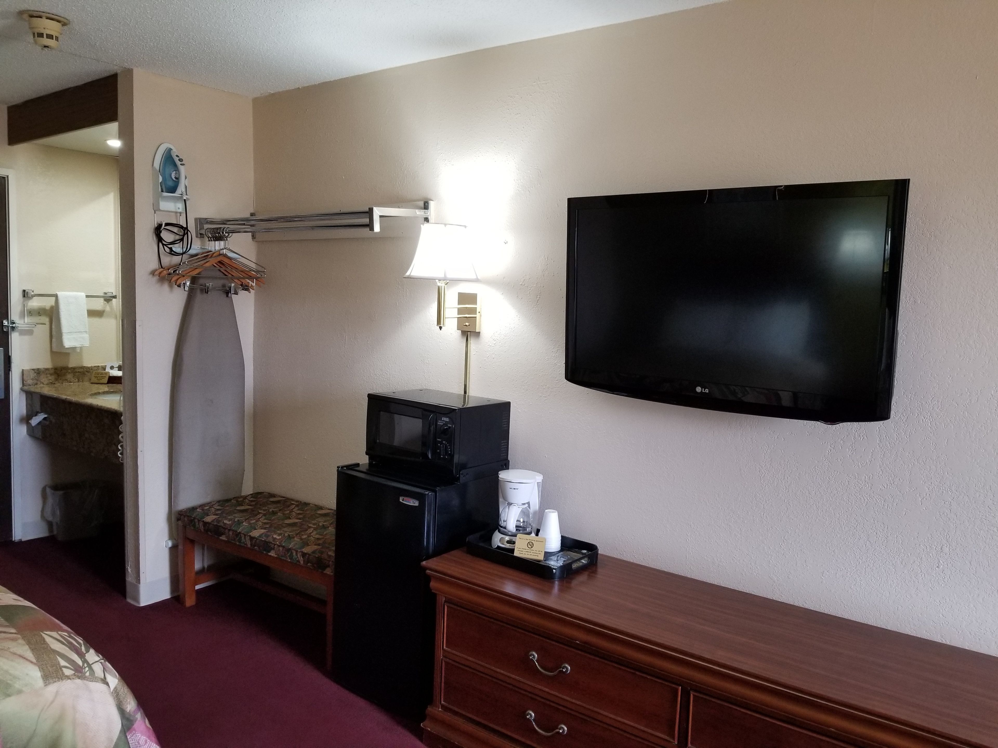 A hotel room with a bed, a desk with a lamp, a microwave, a coffee maker, and a TV.