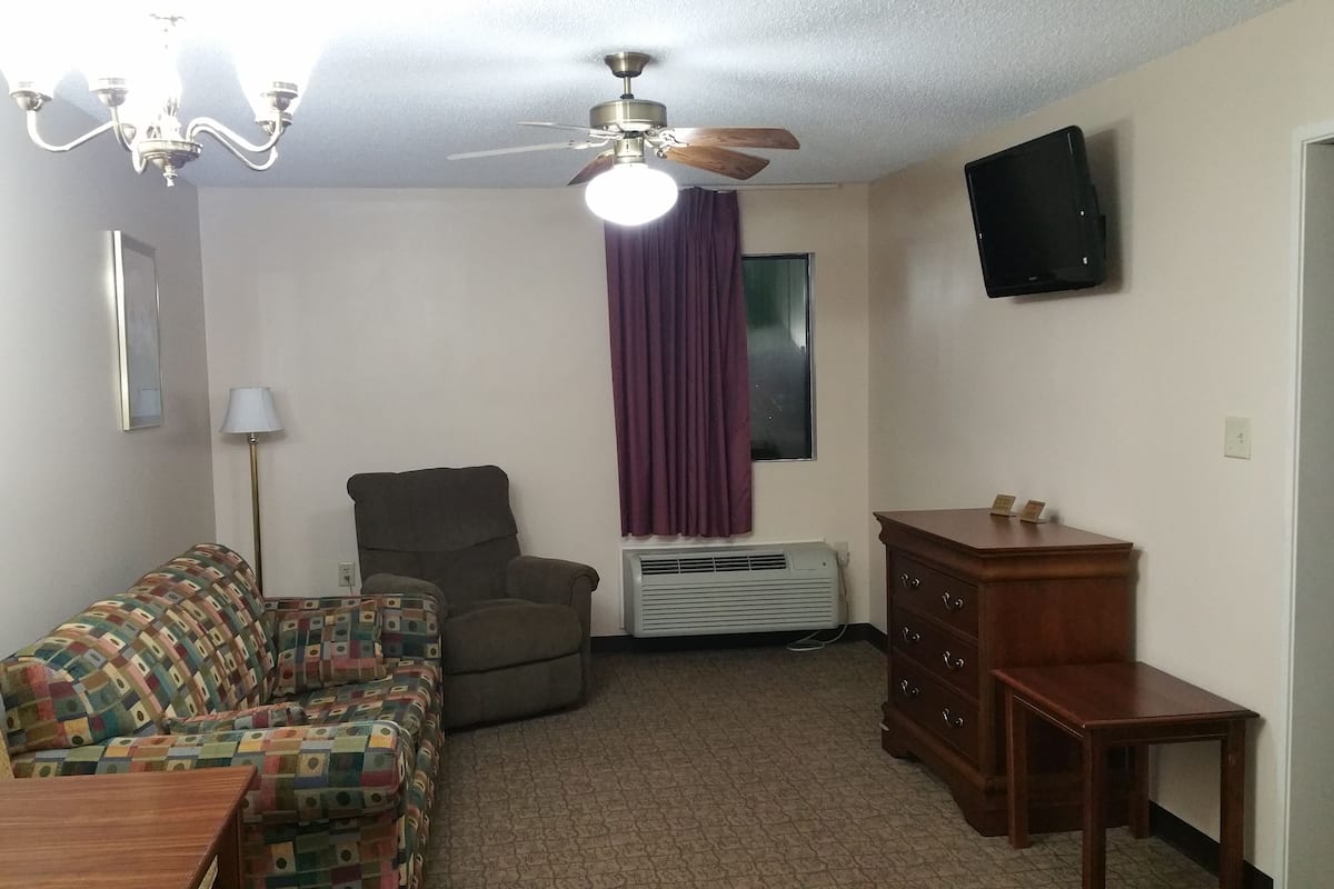 A living room with a sofa, armchair, ceiling fan, TV, and a small table.