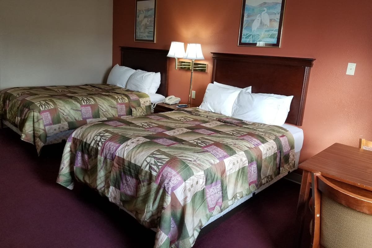 A hotel room with two beds, a nightstand, a lamp, and two wall-mounted paintings.