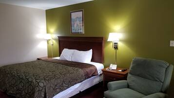 A hotel room with a large bed, two bedside lamps, a green-striped armchair, and a painting on the wall.