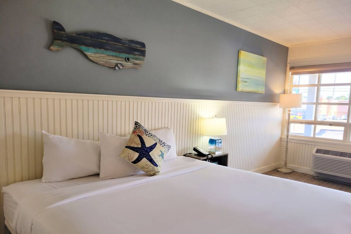 Habitación de hotel con cama, un adorno de pez en la pared, lámpara y ventana.