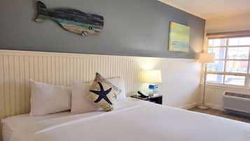 A hotel room with a bed, a wall-mounted fish decoration, a lamp, and a window.